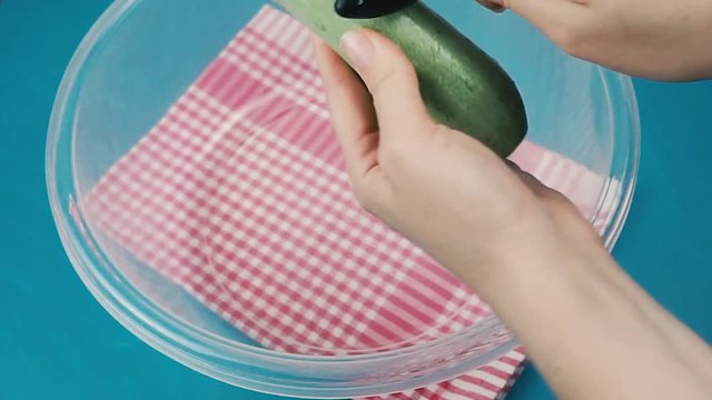 A woman peels cucumber or green pumpkin at kitchen. Close up view of peeling cucumber. Preparing green vegetables 