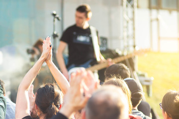 Close-up of the hands of fans clapping to a rock musician on the stage, who performs playing guitar with his band at the open air concert. Fan group, support