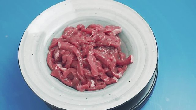Raw meat rotating on blue background. Uncooked fresh meat cut into thin strips. Beef stroganoff in gray plate