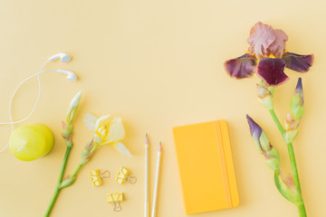 Flat lay blogger or freelancer workspace with a notebook, yellow and brown irises on a yellow background