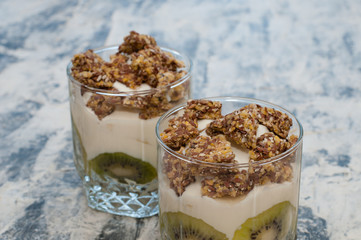 Granola, kiwi, banana and greek yogurt in two glass cups on gray concrete