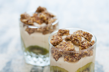 Granola, kiwi, banana and Greek yogurt in two glass cups on gray concrete, close-up macro