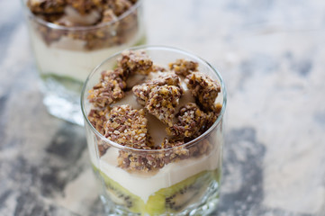 Granola, kiwi, banana and Greek yogurt in two glass cups on gray concrete, copy space. Fitness, figure, body and healthy food
