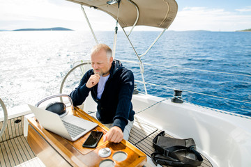 Digitaler Nomade auf einem Segelboot sieht in den Laptop und denkt nach