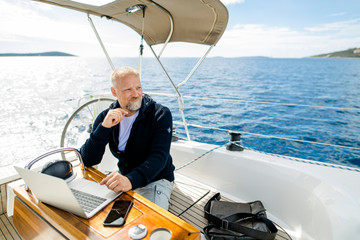 Digitaler Nomade sitzt am Laptop auf einem Segelboot und blickt nach vorne - obrazy, fototapety, plakaty