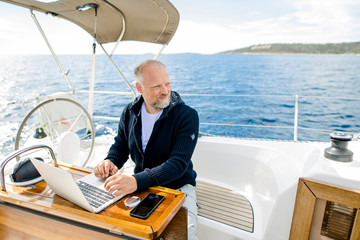 Digitaler Nomade auf einem Segelboot arbeitet konzentriert am Laptop und sieht nach vorne