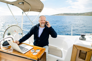 Digitaler Nomade mit Laptop telefoniert glücklich auf einem Segelboot