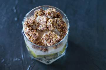 Greek yogurt, granola, banana and kiwi. Dessert in glass beaker on a dark background, close-up macro. Concept body and healthy food