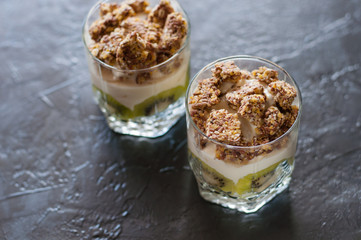Greek yogurt, granola, banana and kiwi. Two desserts in glass cups on dark background. Concept body and healthy food