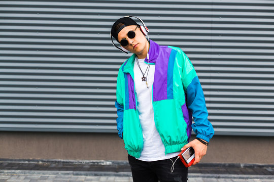 Back in time 90s 80s. Stylish young man in a retro jacket and with a vintage cassette player, on the background of a steel wall, fashion trends, street image