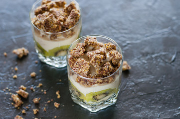 Greek yogurt, granola, banana and kiwi. Desserts in glass cups on dark background, side view from the top. Concept body and healthy food