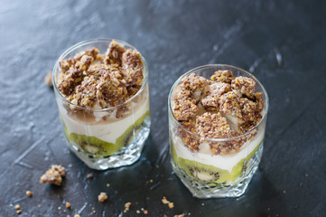 Greek yogurt, granola, banana and kiwi. Desserts in glass cups on dark background, side view from the top. Concept body and healthy food