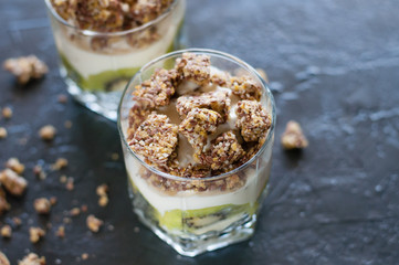 Greek yogurt, granola, banana and kiwi. Desserts in glass cups on dark background, side view from the top. Concept body and healthy food