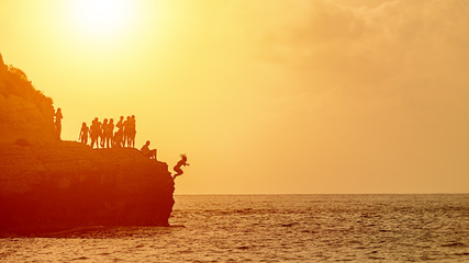 Summer fun with best friends enjoying time together by cliff jumping or cliff diving into ocean at sunset  - 274479969