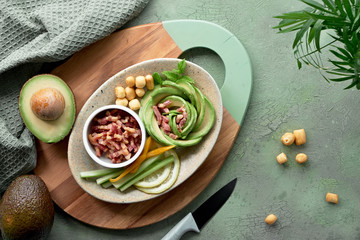 Keto diet, top view of avocado rose salad with bacon cubes and smoked cheese on green table