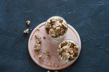 Granola, banana, kiwi and greek yogurt. Dessert in a glass cup on a wooden round board, dark background, flat Lay. Concept body and healthy food