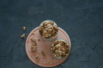 Granola, banana, kiwi and greek yogurt. Dessert in a glass cup on a wooden round board, dark background, flat Lay. Concept body and healthy food