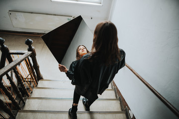 portrait of brunette woman walking down the stairs while holding a mirror