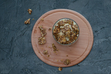 Granola, banana, kiwi and greek yogurt. Dessert in glass cup on a wooden round board, dark background. Concept body and healthy food