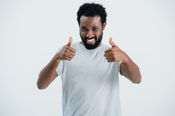 smiling african american man in grey t-shirt showing thumbs up isolated on grey