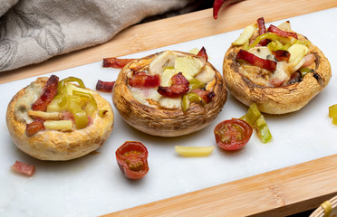 Delicious mushrooms (champignon, foot cut, Agaricus Bisporus) cooked and stuffed (bacon, tomato, garlic, pepper, ...). Close up.