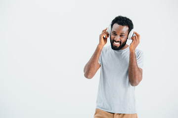 cheerful african american man listening music with headphones, isolated on grey