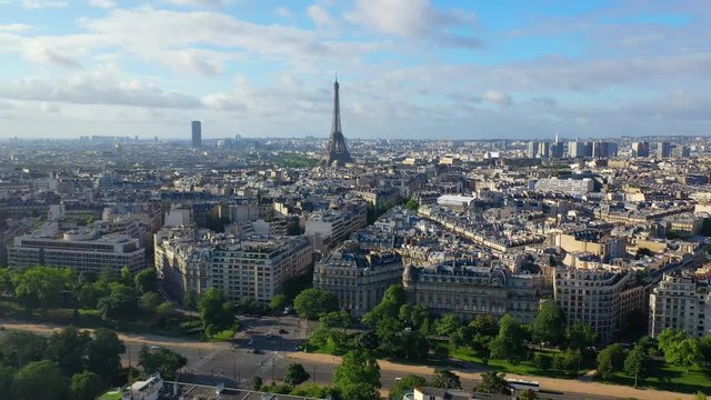 Aerial, drone shot, tilting towards the Eiffel tower, overlooking traffic on french streets, buildings and architecture, in the city of Paris, on a sunny, summer day, in France