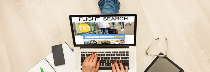 Young woman working on laptop computer, searching for flight using online web service. Attractive female booking round trip airplane ticket on website. Rear view over the shoulder. Focus on screen