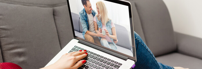 High angle over the shoulder view of the hands of a woman typing on a laptop computer as she sits on the carpet at home