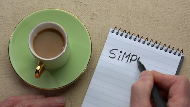 Simplify word - man hand writing a note with a black marker in a spiral notebook, overhead view