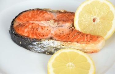 piece of sturgeon fish with skin, and a slice of limrna on a white plate