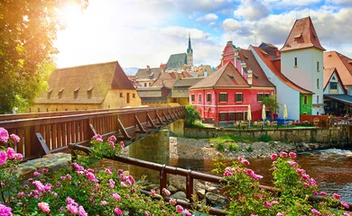 Poster Czech Krumlov, (Cesky Krumlov), Czech Republic. Wooden bridge over river Vltava. Vintage picturesque old town with colorful houses and chapel of church. Rose flowers on bank. Sunny summer day. © Yasonya