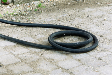 A black twisted hose lies on the ground. Fuel hose