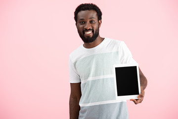 smiling african american man showing digital tablet with blank screen isolated on pink