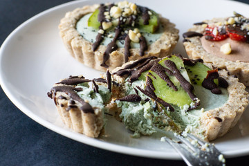 Raw vegan tartlets on the white plate. Healthy desserts, close up
