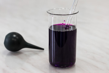 measuring cup with a purple substance, potassium permanganate, with a pipette. Near black medical pear. Everything is on the table in the lab