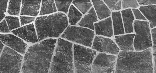 High resolution full frame background of a wall made of old and weathered stone slates in black and white. Copy space.