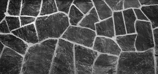 High resolution full frame background of a wall made of old and weathered gray stone slates in black and white with vignetting. Copy space.