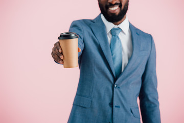 cropped view of smiling african american businessman holding coffee to go, isolated on pink