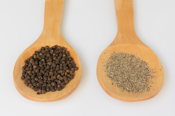 Una  cuchara  de madera  con pimienta negra en grano  y otra molida