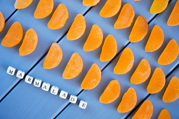 Fruit marmalade in the form of parts of the mandarin lies on the painted boards. The combination of blue and orange. Signature and letters