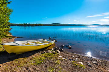 Fototapeta na wymiar The motor boat in the border of Siebdniesjavrrie lake Swedish Lapland. The sun is reflecting in the water. Vasterbotten county, Norrland, Sweden.