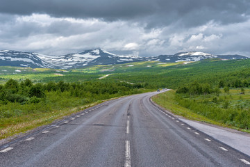 National road 95 in Sweden in approach of Norwegian frontier Merkenisvuopmekietje. Tundra forest valleys and Scandinavian mountains partially hided with clouds are at background.