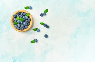 Fresh blueberries in a wooden bowl on a light background, top view