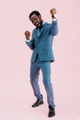 excited successful african american businessman in suit, isolated on pink