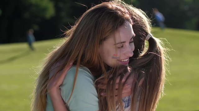 Close-up portrait of happy homosexual couple with rainbow lgbt flag painted on cheeks hugging each other outdoor. Joyful lovers enjoying embrace and summer leisure, gentle wind waving their long hair