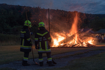 2 Feuerwehrmänner überwachen ein traditionelles Sonnwendfeuer