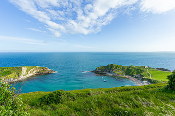 Fototapeta na wymiar A view of the Lulworth Cove along the Jurrassic Coast in Dorset under a majestic blue sky and some white clouds.