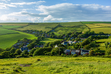 A view of a rural village (West Lulworth) from the hill under a majestic blue sky and some white...