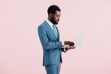african american businessman using laptop isolated on pink